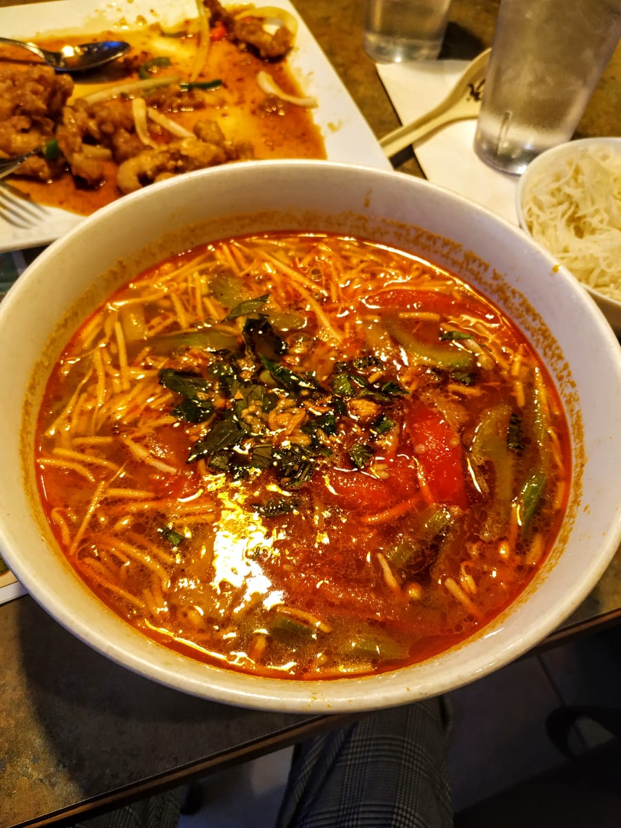 A bowl of noodle soup in a red, spicy broth with green onion
